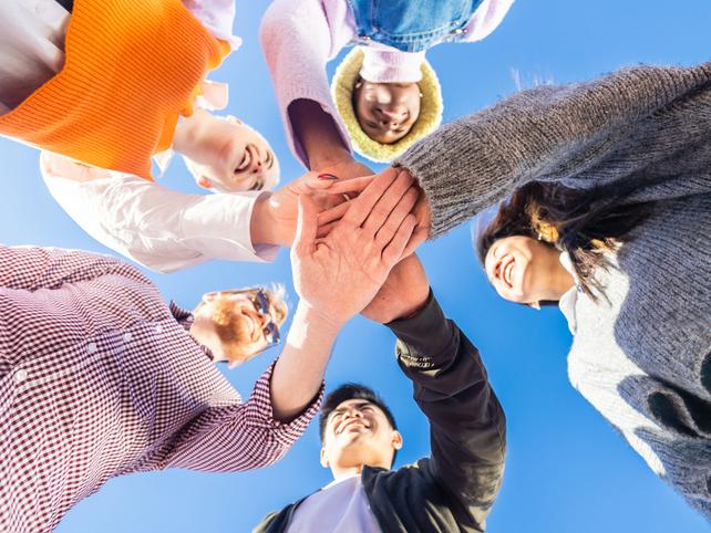 Group of young people in a circle all joining hands in the centre