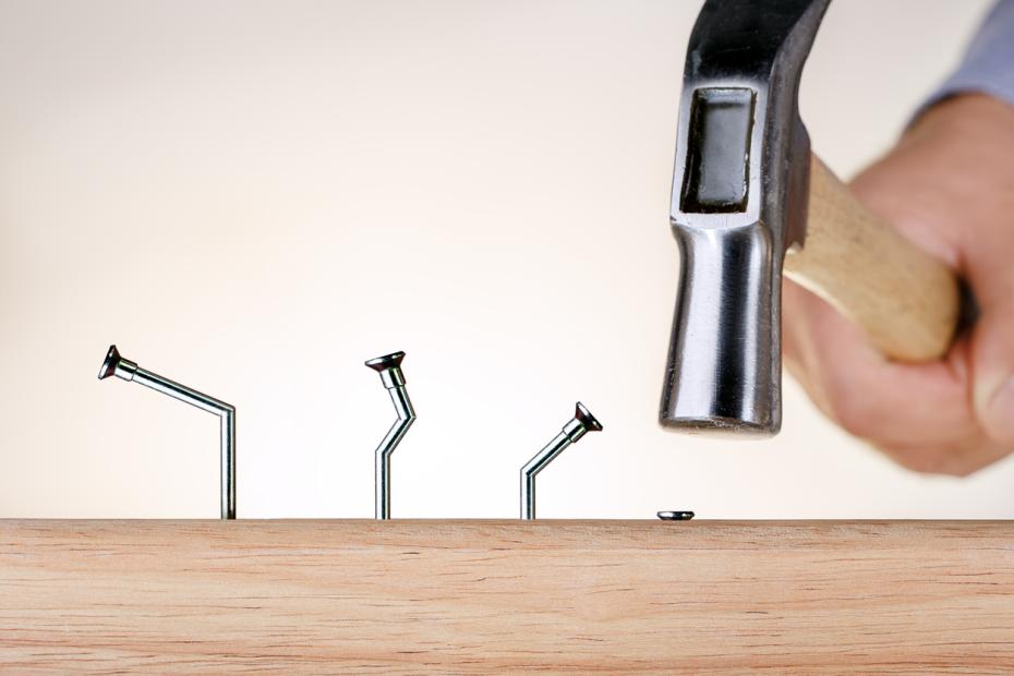 A hammer next to a series of bent nails and one perfectly hammered in