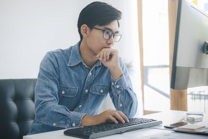 Asian man concentrating on writing at a computer