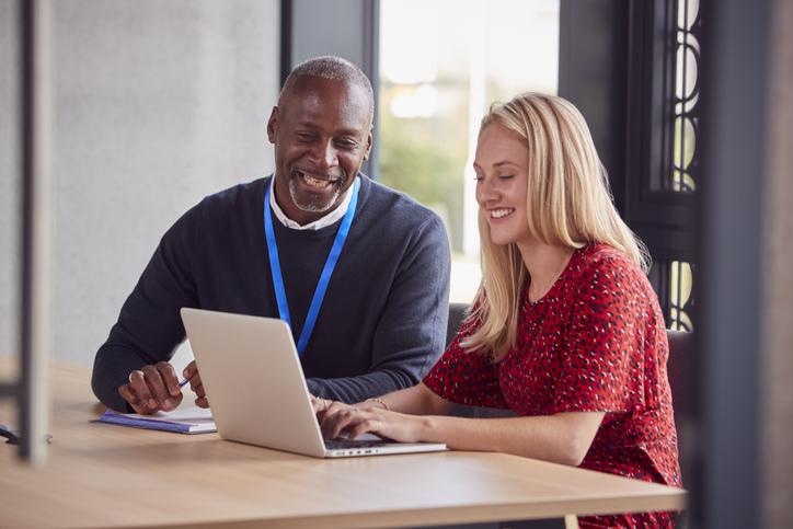 A professor laughs with a student over a laptop