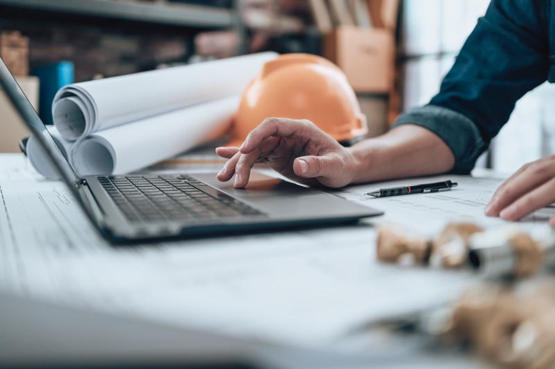 Laptop, hard hat and blueprints on desk