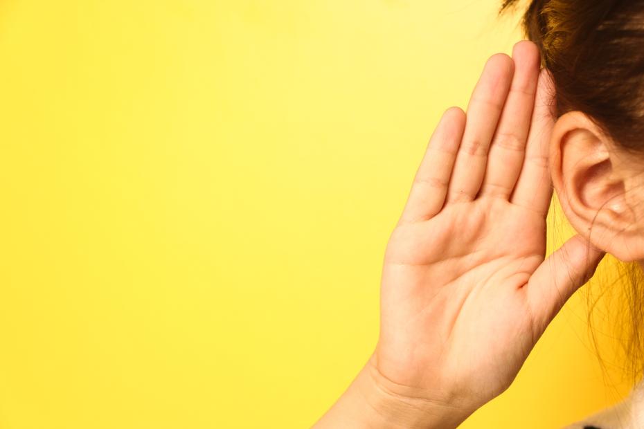 The left hand side of a woman's face with her hand held up against her ear