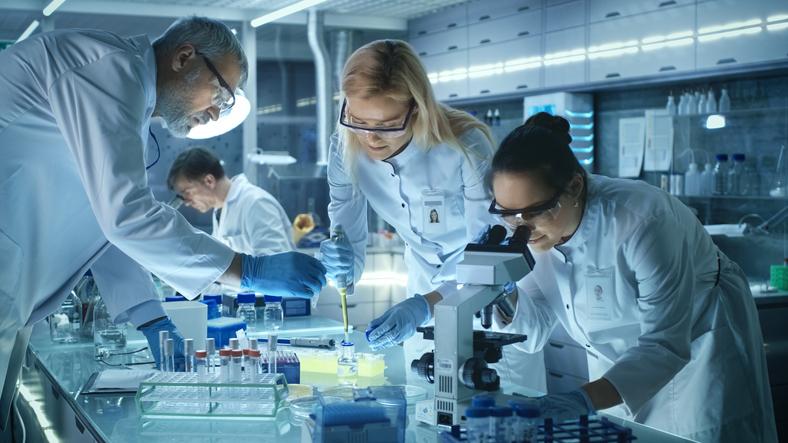 Three scientists in white coats converse in a laboratory