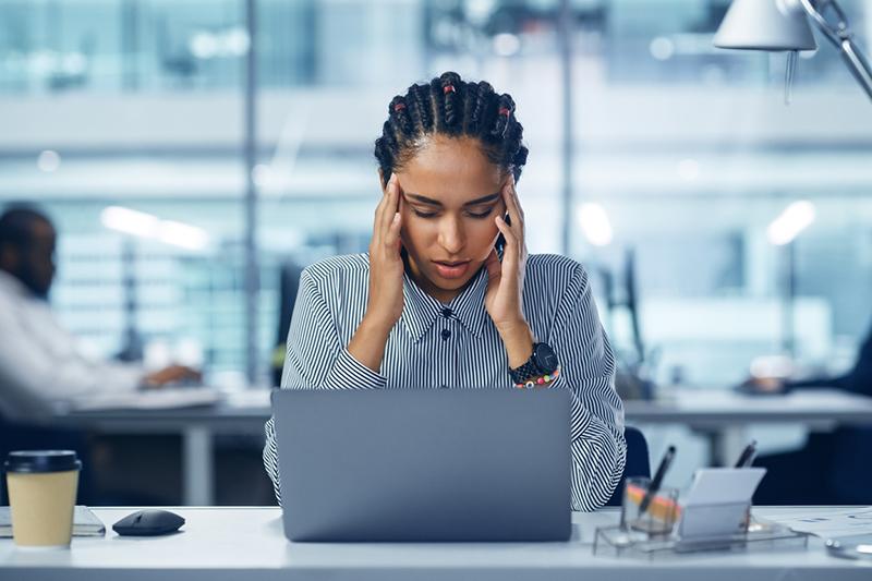 Young black woman rubs temples at laptop, frustration