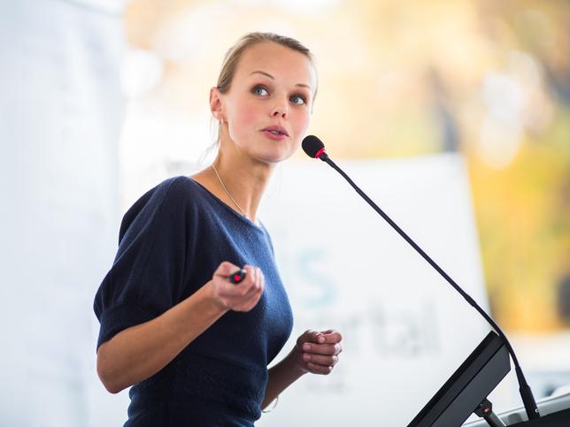 A woman makes a speech, talking into a microphone and using a laser pointer