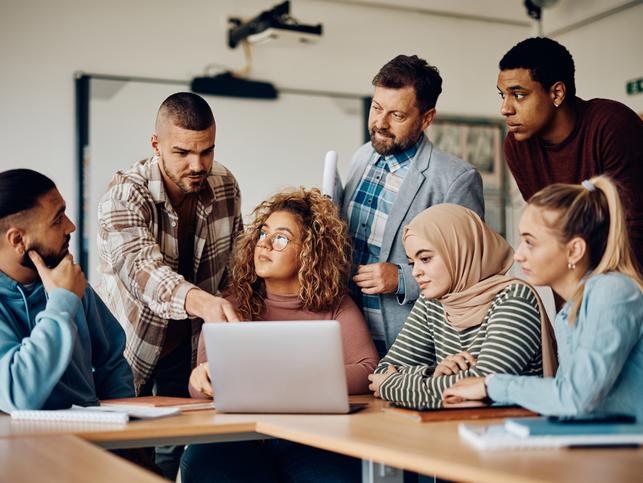 A group of students gather round a laptop