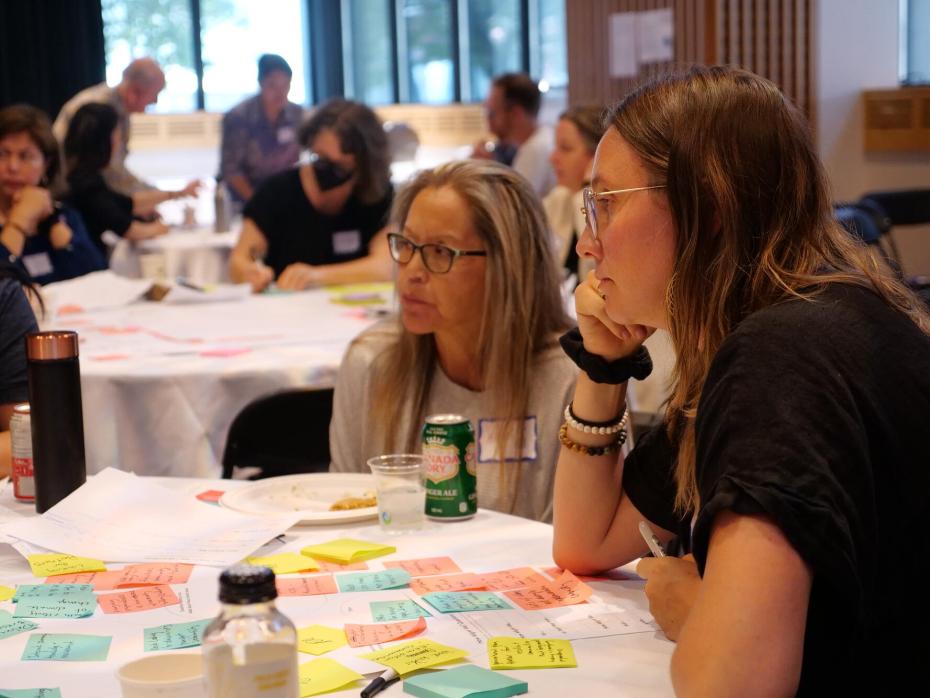 Two people sit at a table covered with post-it notes at an event