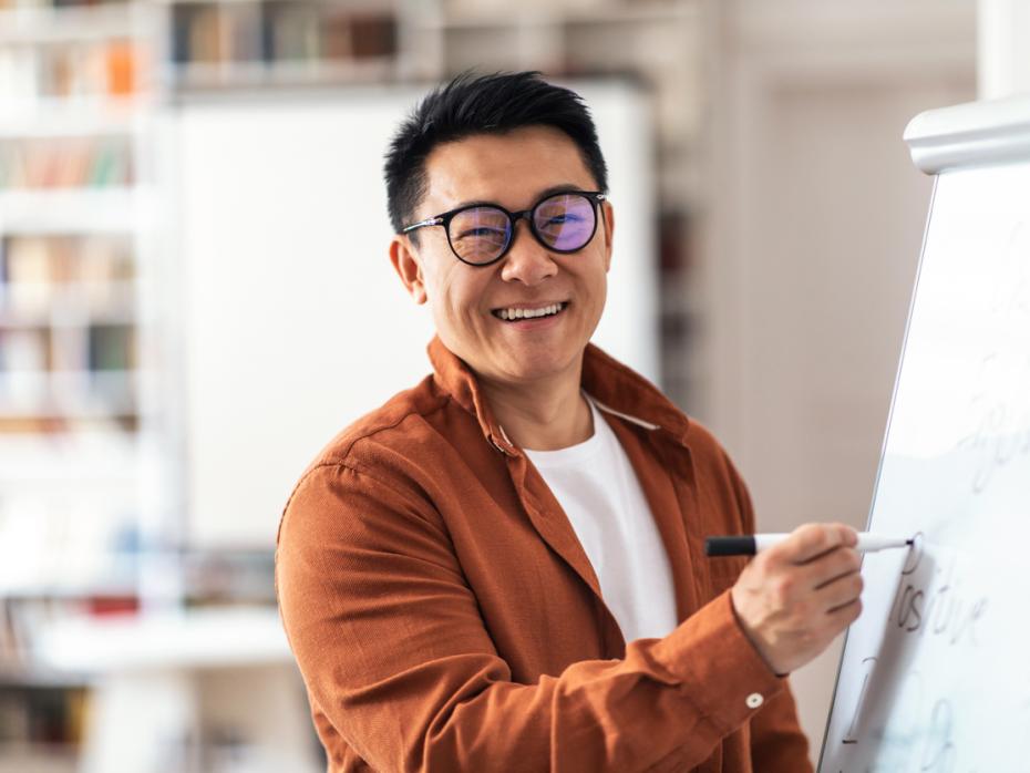 Professor smiling at the camera while writing something on a whitebord