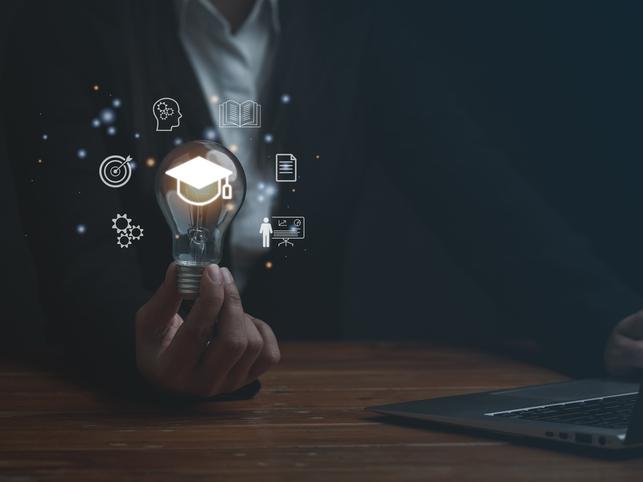 A woman holds a lightbulb with a holographic rendition of a mortarboard,