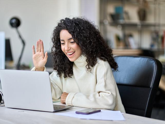 A woman waves to others over a video call