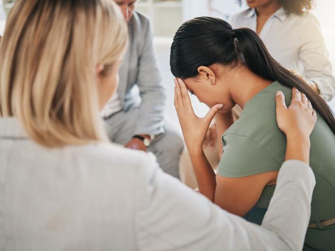 A group comforts a woman, sitting with her head bowed