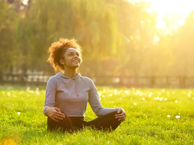 A smiling woman sits in a park, basking in sunshine