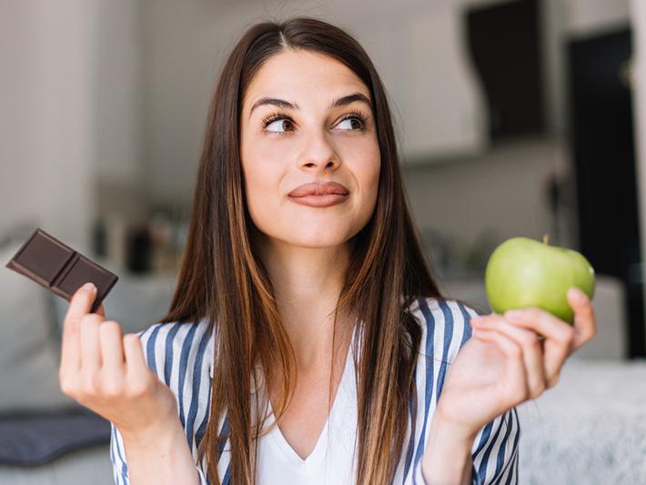 Woman choosing between chocolate and apple