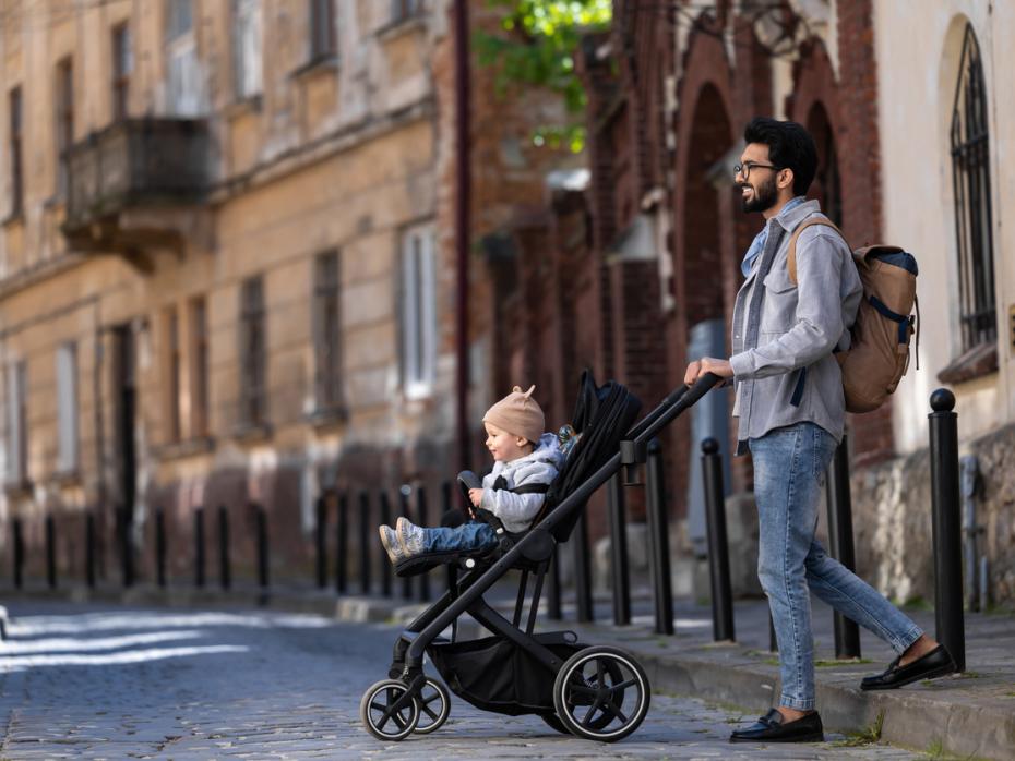 Student father pushing a pram across the street