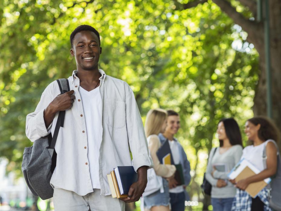 A Black student walking around campus with books in hand