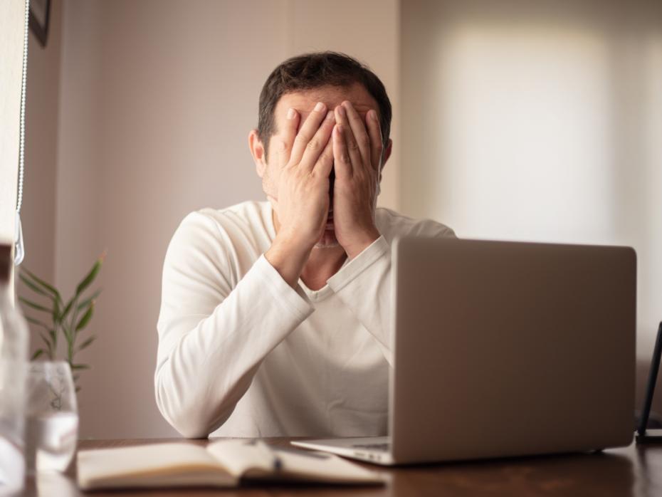 Man covering his eyes in front of his laptop