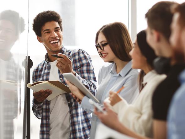 Students laugh together while working on a whiteboard