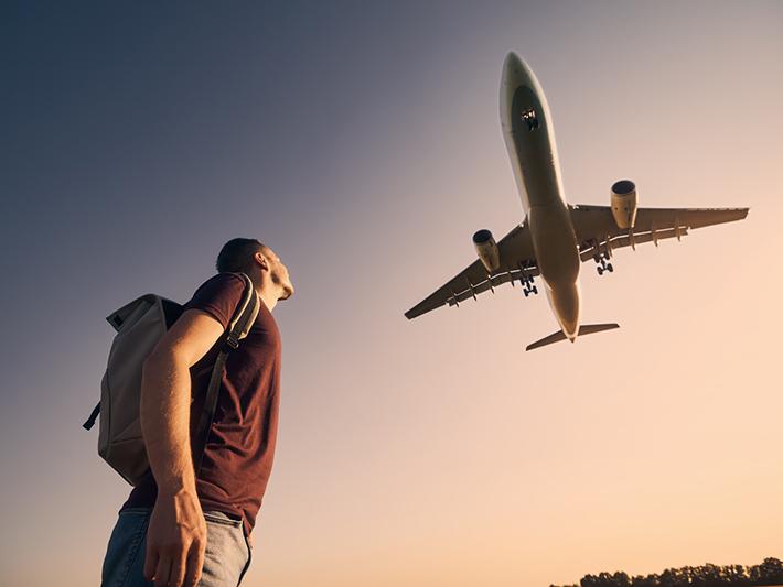 Young male with backpack looking up at a plane overhead