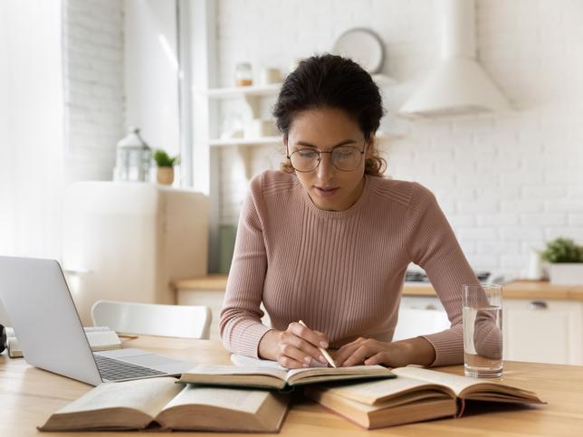 A woman works on an essay, using her laptop and several books