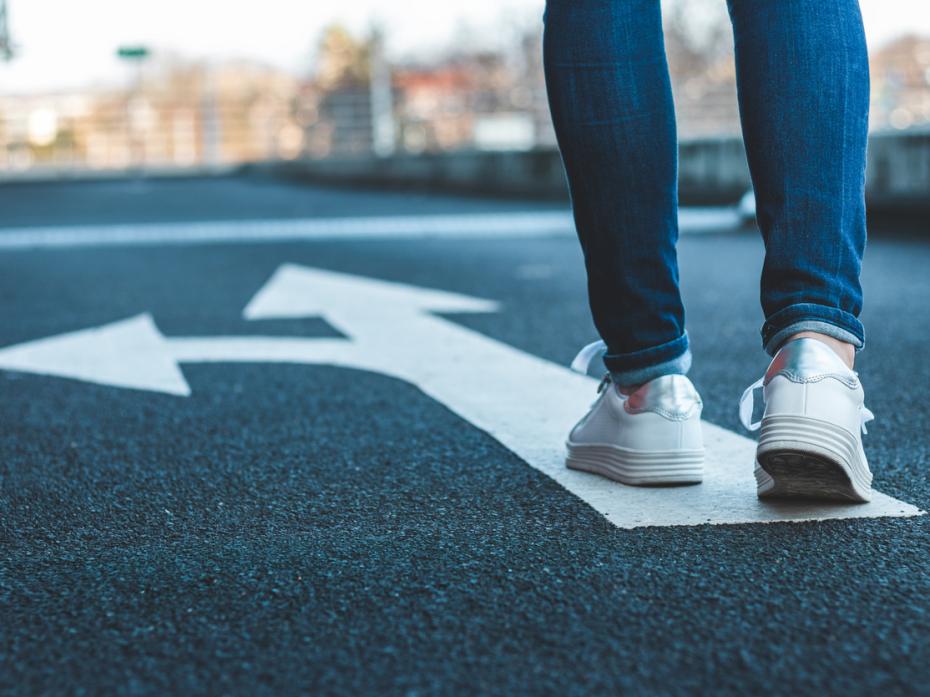 A pair of legs following an arrow on asphalt