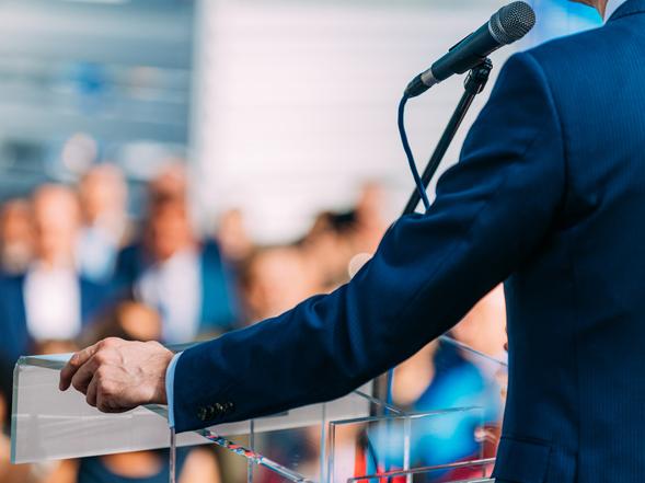 A speaker stands at a lectern with a microphone