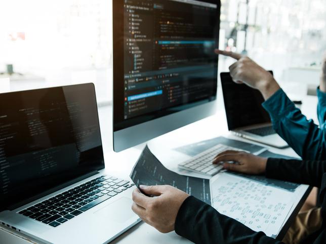 Two software engineers gesture at multiple screens