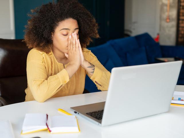 A young woman takes a deep breath at a laptop