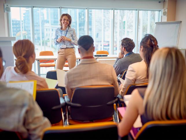 A group of people listen to a lanyard-wearing speaker