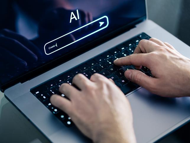 Hands type on a laptop with "AI" on the screen