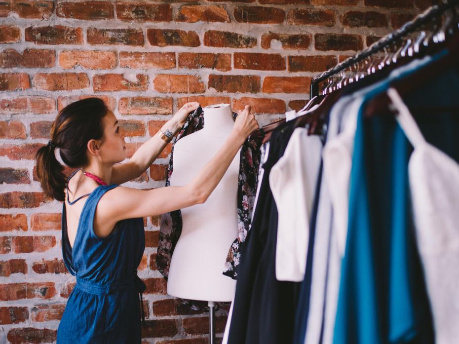 A woman putting a shirt on a mannequin next to clothes rails