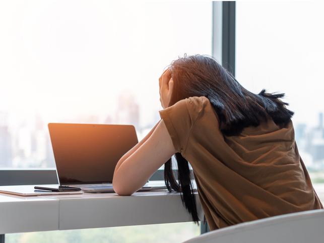 A woman holds her head in her hands over a laptop screen