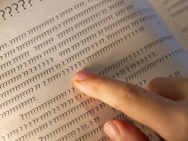 A finger follows text in a book written in question marks