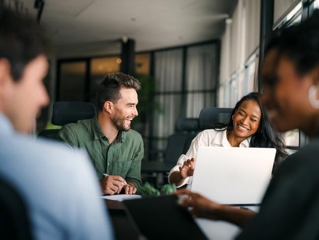 Colleagues laugh together over a laptop