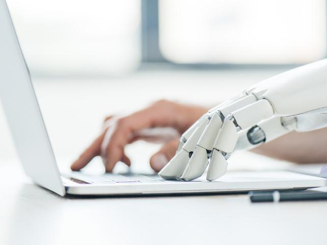 A robot hand types at a laptop