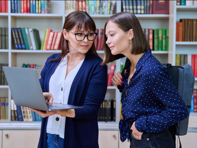 A librarian helps a student, using a laptop