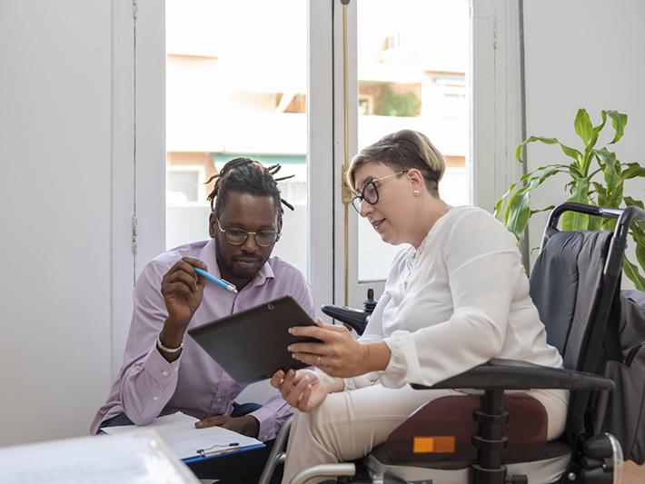 Woman in wheelchair and young black man looking at tablet