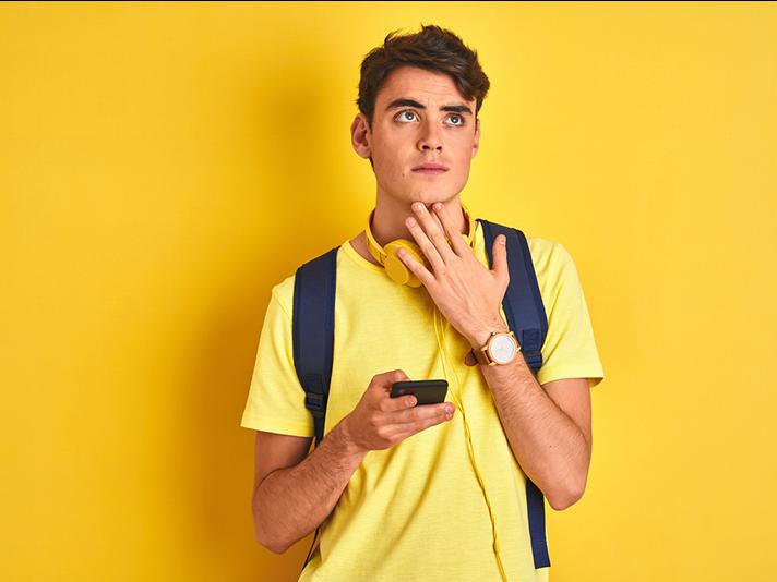 Young male student looking perplexed with mobile phone