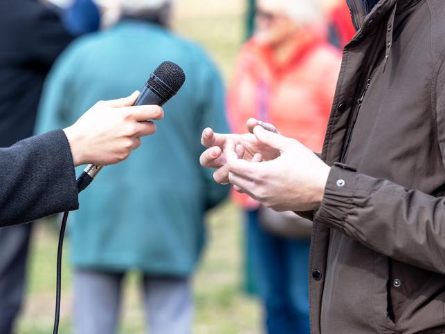 A journalist interviews a man in a raincoat