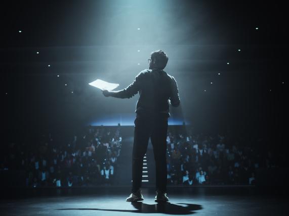 A lecturer is illuminated by the stage lights