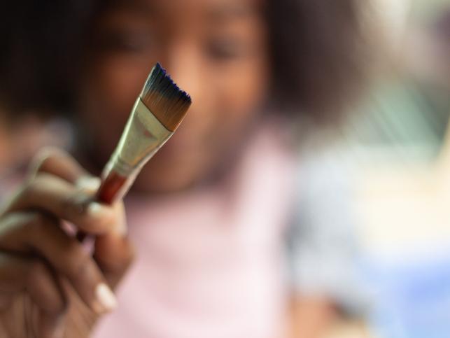 A Black artist holds a paintbrush out to the camera