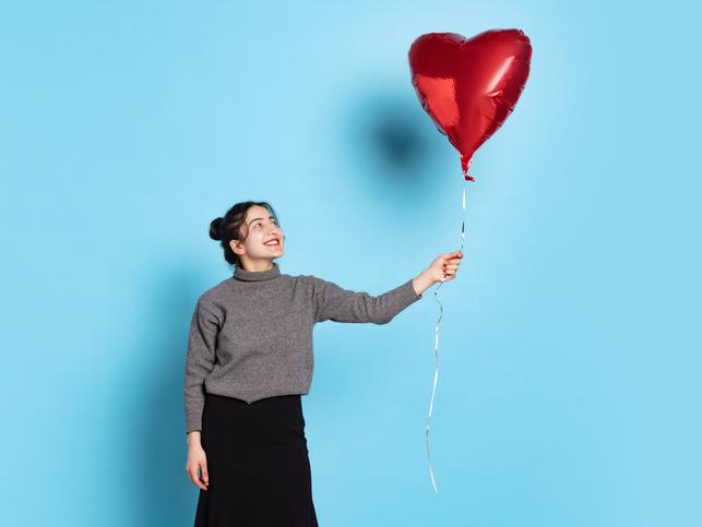 A smiling woman holds a red, heart-shaped helium balloon