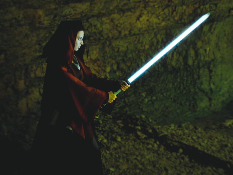 A woman wearing a cape with a light saber in hand, ready for battle