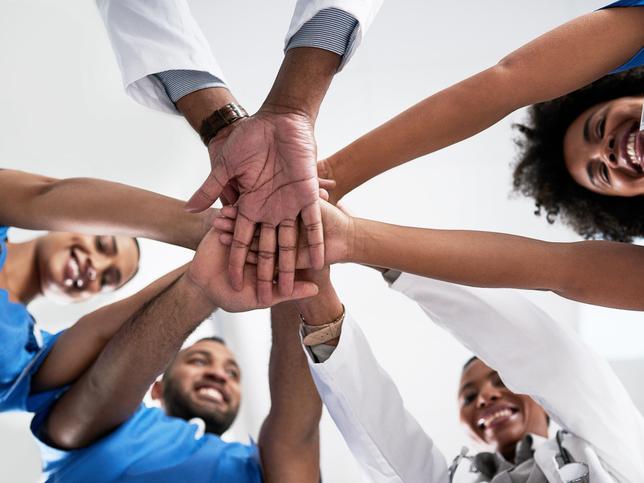 Doctors of colour clasp hands in a circle