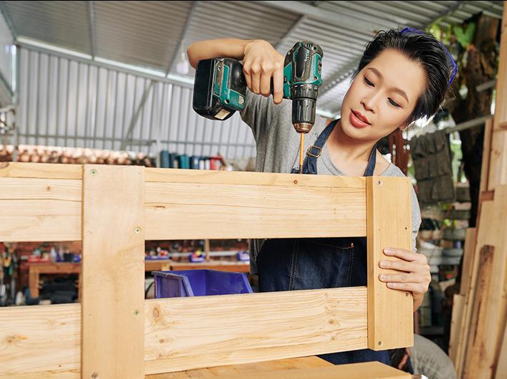 Young woman with a drill assembling a wooden bookcase