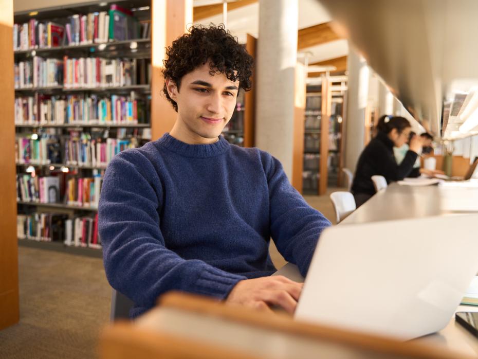 A male student working on his laptop in the library