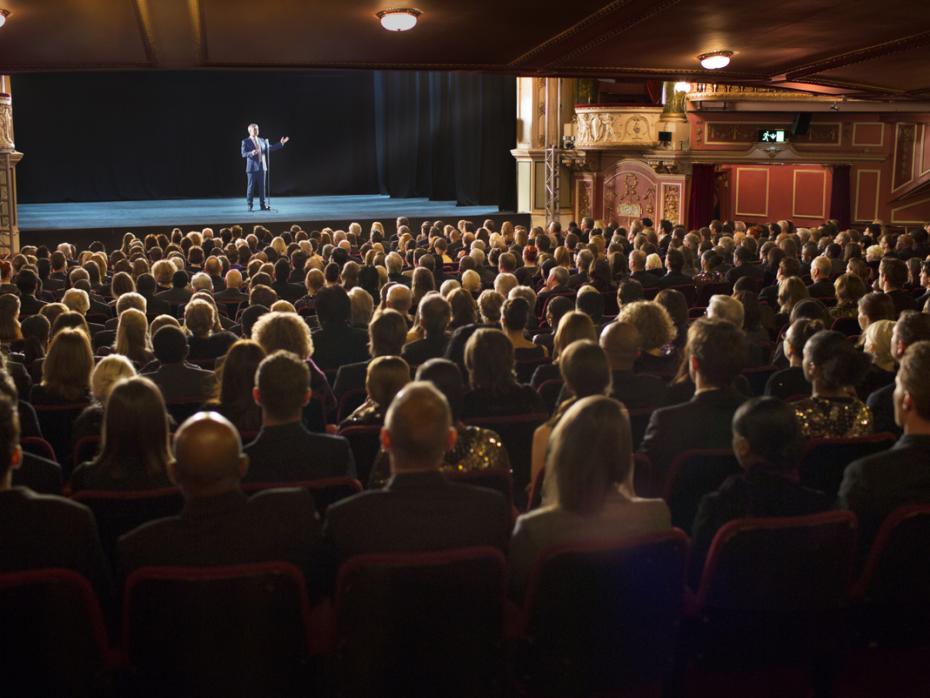 An audience watching a man on stage in a theatre