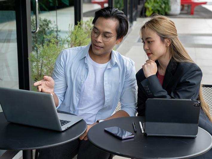 Two Asian students in a coffee shop looking at a laptop