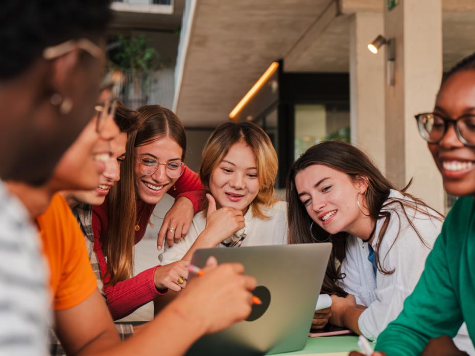 A group of students interacting happily around a laptop