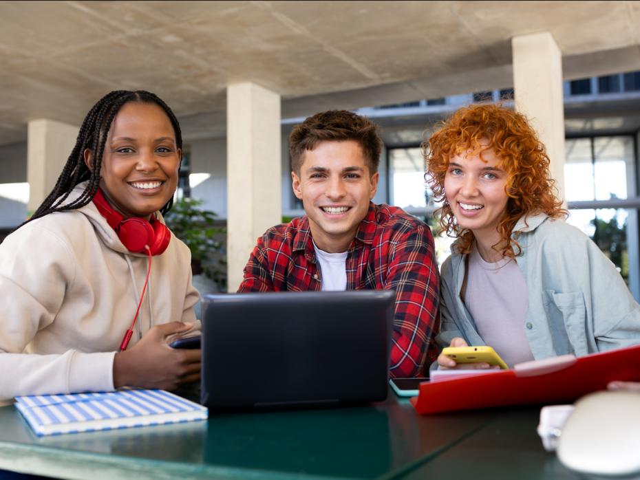 Three students working from a laptop smiling to camera