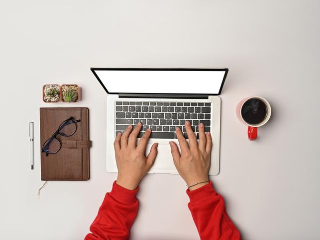 Hands type at a laptop, as seen from above